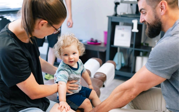A child receives a chiropractic or therapy treatment with assistance from two adults.